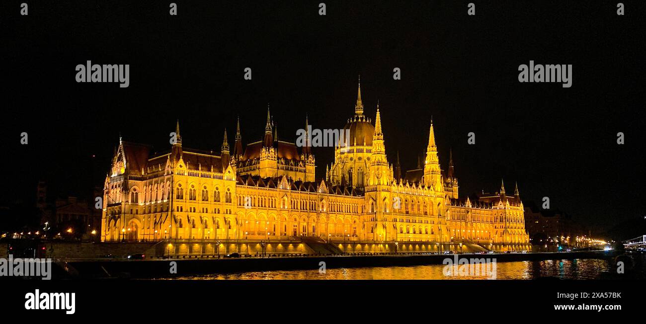 Nächtliche Bootstour vorbei am Budapester Parlamentsgebäude, beleuchtet bei Nacht. Ein wunderschönes Gebäude mit goldenen Lichtern am Rande des Stockfoto