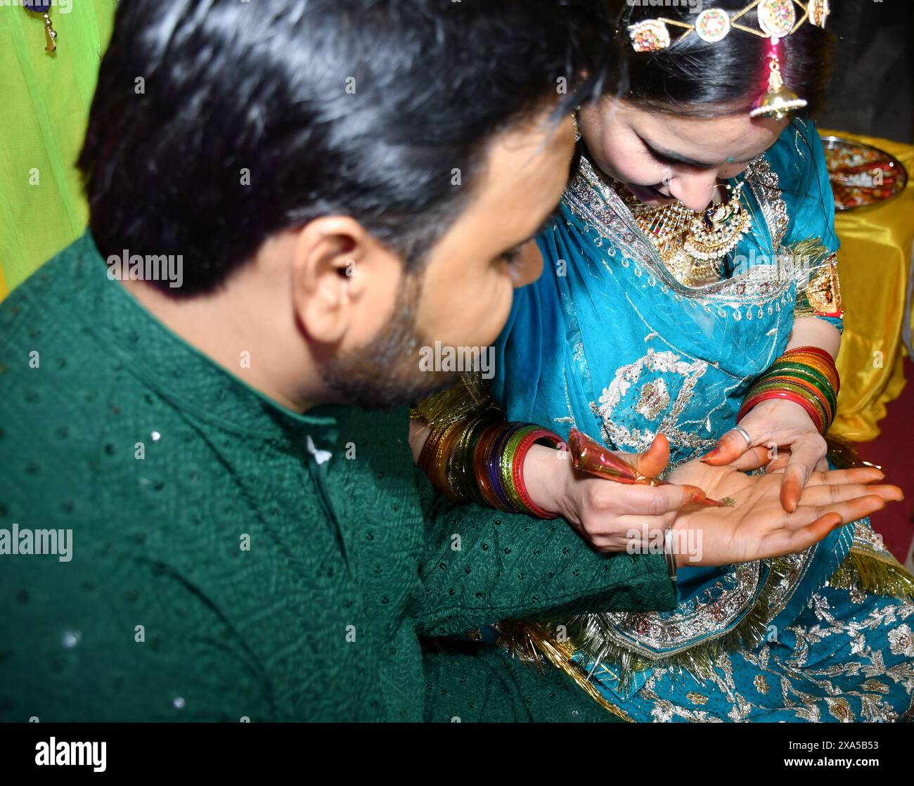 Zwei Leute stehen mit Händen, die sich berühren, halten ein Objekt in einer Mehndi-Zeremonie zusammen Stockfoto