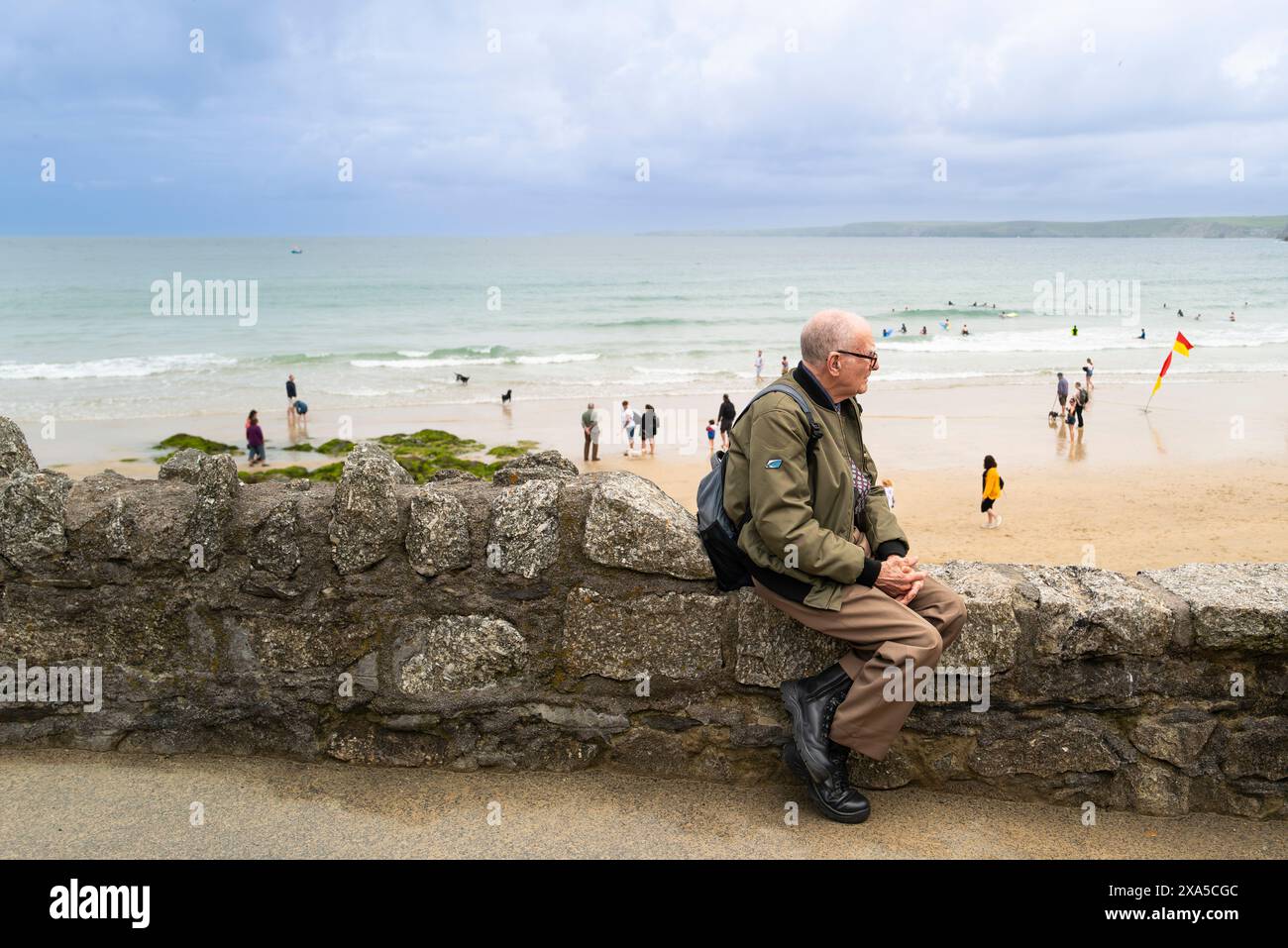 Ein reifer männlicher Besucher, der auf einer Mauer mit Blick auf Towan Beach an der Küste von Newquay in Cornwall in Großbritannien sitzt. Stockfoto