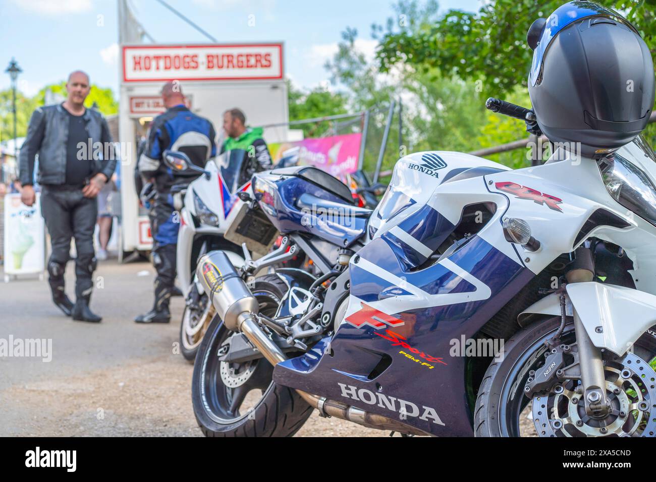 Nahaufnahme eines Honda-Motorrads mit Fahrern im Hintergrund an einem Hot Dog & Burgers Stand, der Erfrischungen auf einer lokalen britischen Sommerveranstaltung/-Messe kaufte. Stockfoto