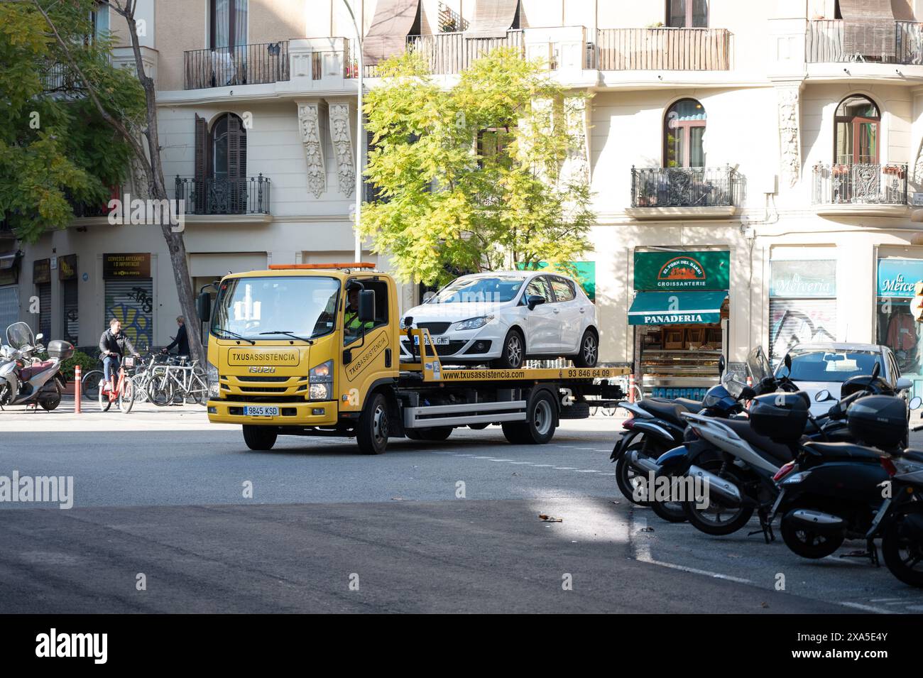 Ein gelber Isuzu M21-Kranwagen lädt einen beschädigten Ibiza-Sitz der vierten Generation auf die hintere Plattform. Stockfoto