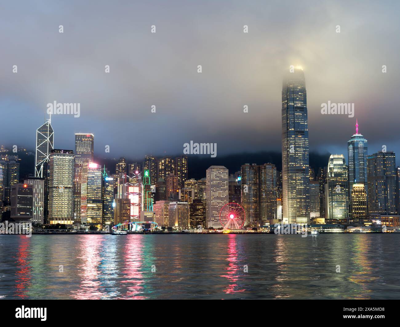 Ein Blick auf die Skyline des Hafens von Hong Kong Victoria bei Nacht mit den hohen Wolkenkratzern, die in niedrige Regenwolken stürzen Stockfoto