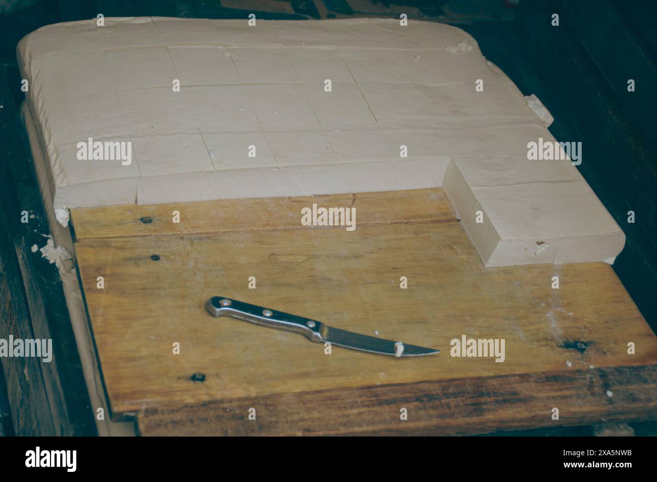 Tofu oder Tahu auf dem Holzschneidetisch, der mit einem kleinen Messer in Quadrate geschnitten wird, ein traditionelles lokales Produkt aus Samosir North Sumatra, Indonesien Stockfoto