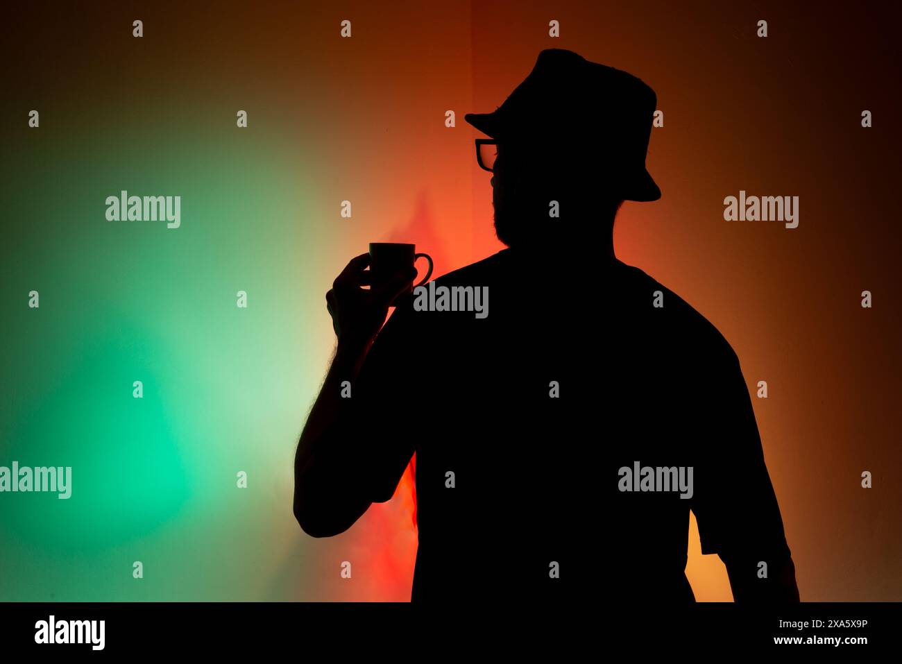 Mann mit Hut in Silhouette hält eine Tasse Kaffee vor bunter Hintergrund. Stockfoto