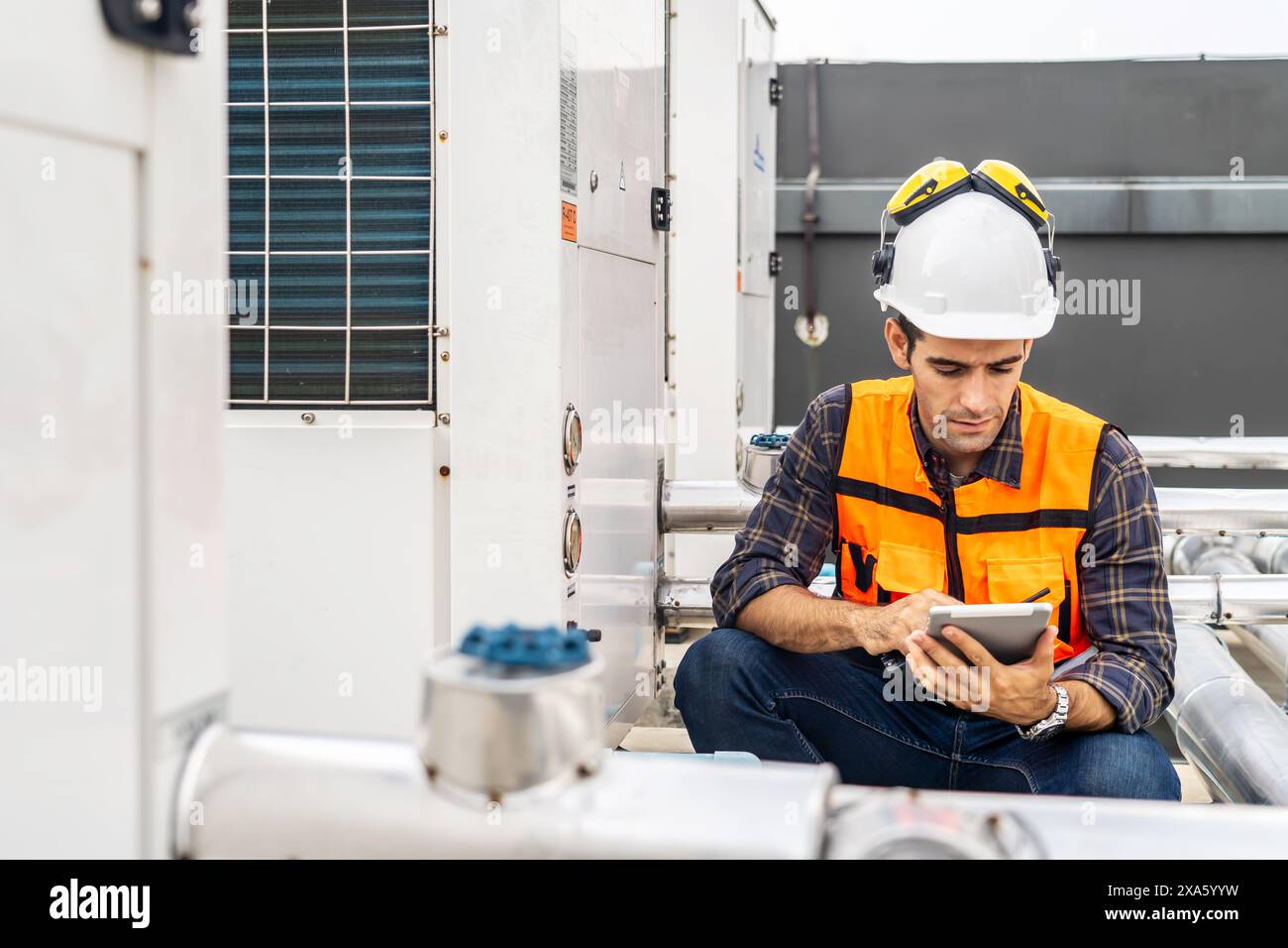 Ein Bauarbeiter in einem Schutzhelm, der im Sitzen ein digitales Tablet verwendet Stockfoto