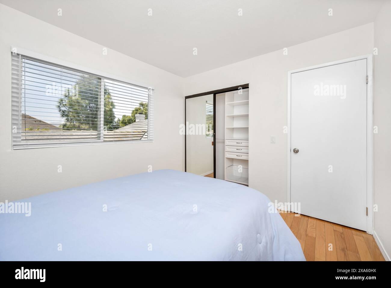 Innenraum des Schlafzimmers mit Bett, Kleiderschrank, Tür und großen Fenstern Stockfoto