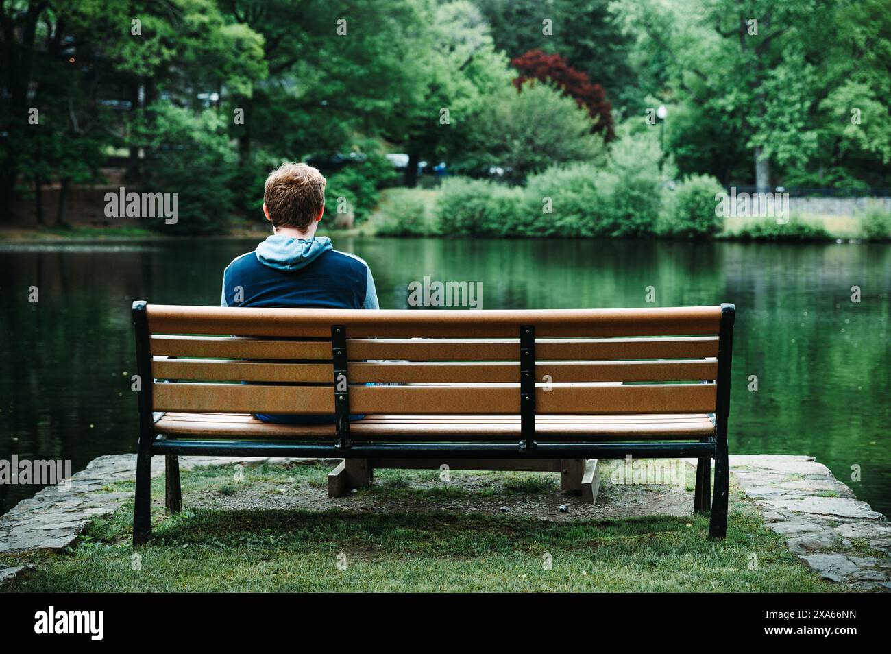 Ein Mann sitzt auf einer Holzbank an einem ruhigen See Stockfoto