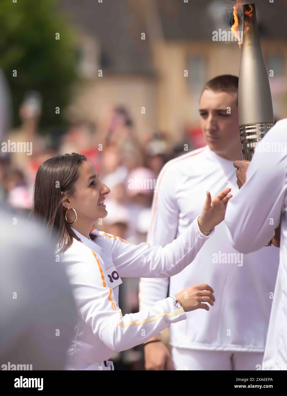 Eine Frau übergibt die Olympische Flamme von Paris 2024 auf dem Stadtplatz in Sainte-Mère-Eglise, Normandie, als Teil des Relais de La Flamme vom 31. Mai 2024. Fackelträger marschierten durch das Dorf, als die Feierlichkeiten vor dem D-Day 80 stattfanden. Gedenkveranstaltungen wie diese dienen dazu, die Opfer zu ehren, die US-Mitglieder vor 80 Jahren zur Sicherung von Frieden und Sicherheit gebracht haben, und zukünftige Generationen dazu zu inspirieren, eine kollektive Vision des Weltfriedens zu schätzen. Stockfoto