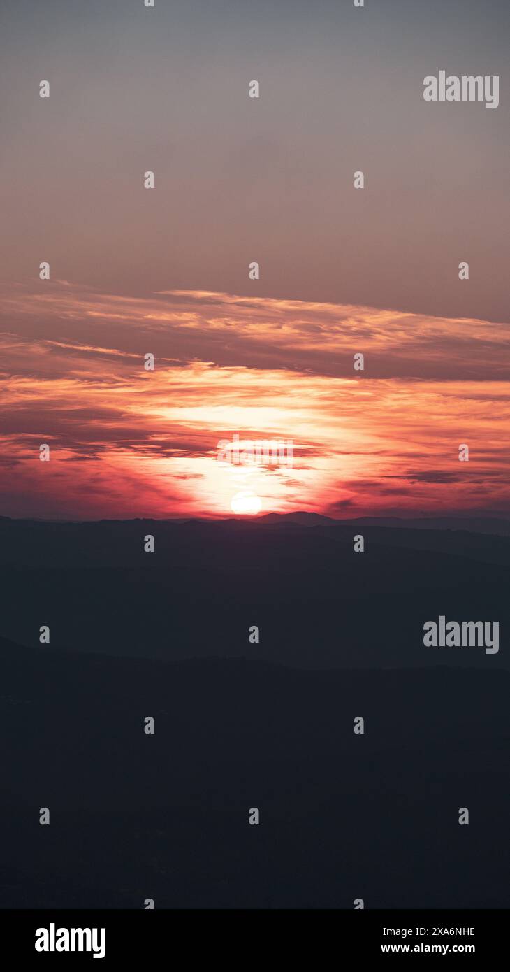 Der Sonnenuntergang über fernen Bergen, kleine Wolkenlinie am Himmel. Stockfoto