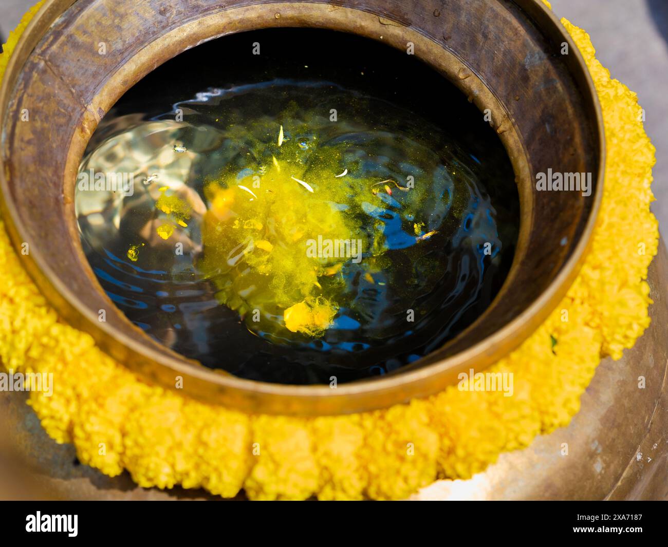 Eine Schüssel gefüllt mit haldi-Wasser draußen mit blühenden Blumen auf einem Tisch Stockfoto