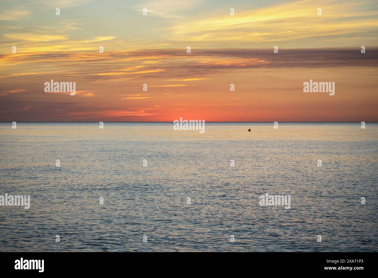 Ein Sonnenaufgang am Strand mit Wolken in leuchtenden Farben, die sich vom Meer reflektieren und eine perfekte Sonnenuntergangsszene für Hintergrundbilder und Urlaubshintergründe schaffen. Stockfoto