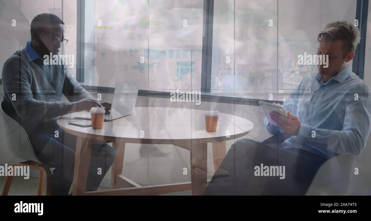 Bild eines afroamerikanischen Mannes, der am Laptop arbeitet, während der kaukasier Tablette liest Stockfoto