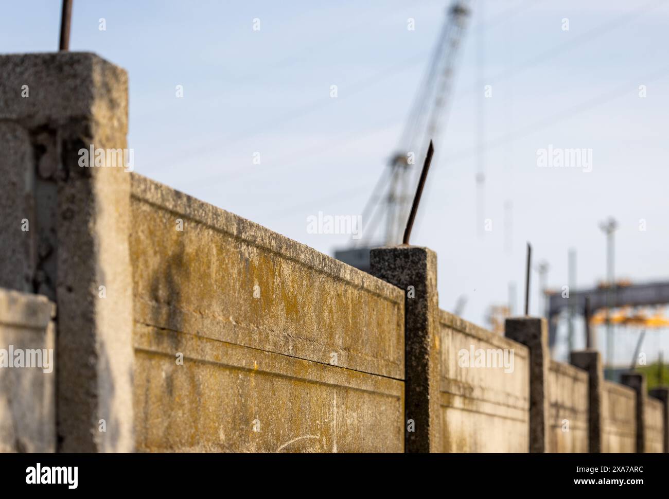 Eine Betonwand mit mehreren Pfählen und Kränen im Hintergrund Stockfoto