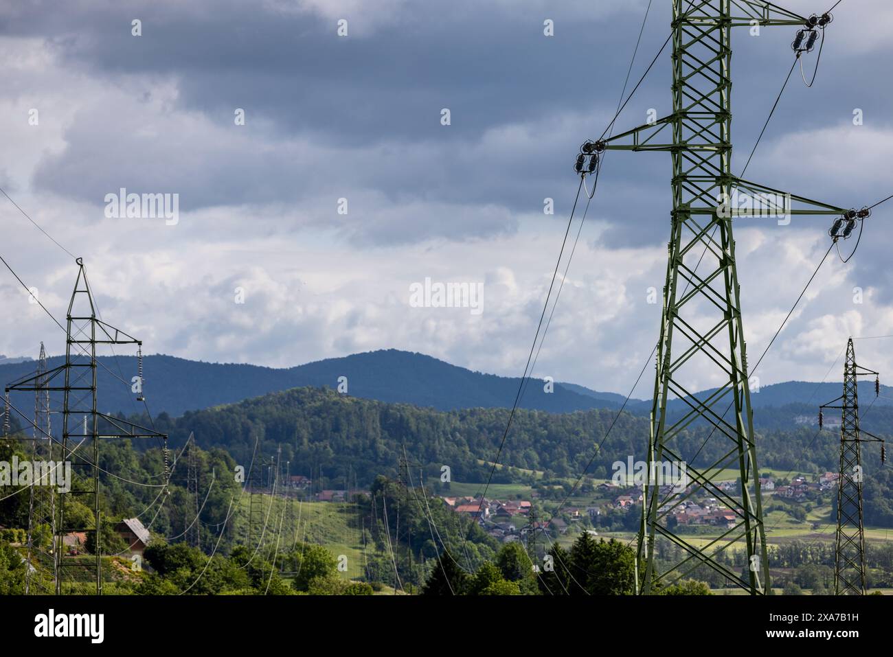 Ein Schuss von Stromleitungen über grasbewachsenem Feld und Hügeln in der Nähe von Wasser Stockfoto