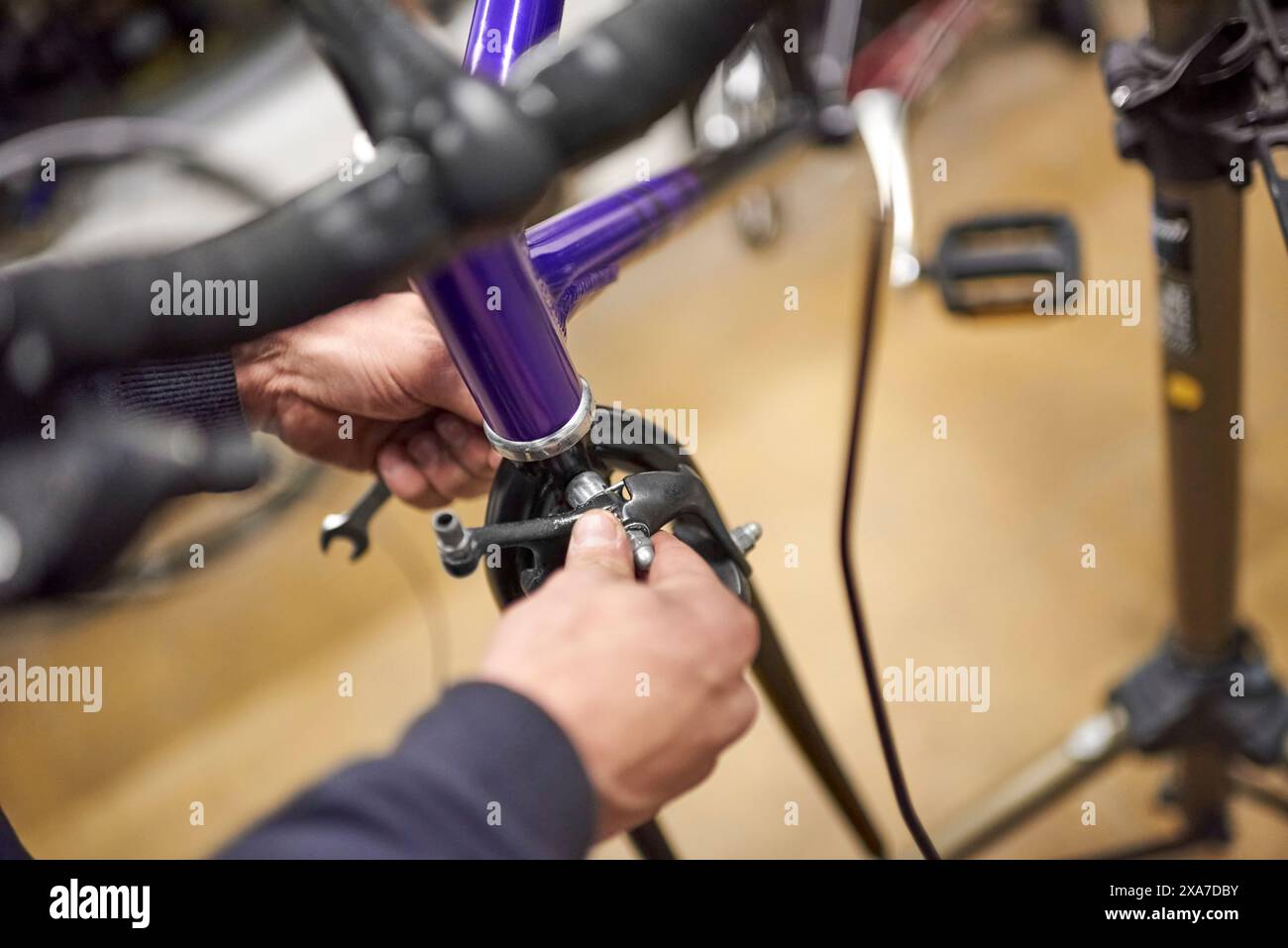Unbekannter Mann, der die Bremsanlage eines Fahrrads im Rahmen der Wartungsarbeiten, die er in seiner Werkstatt durchführt, montiert. Echte Menschen bei der Arbeit. Stockfoto