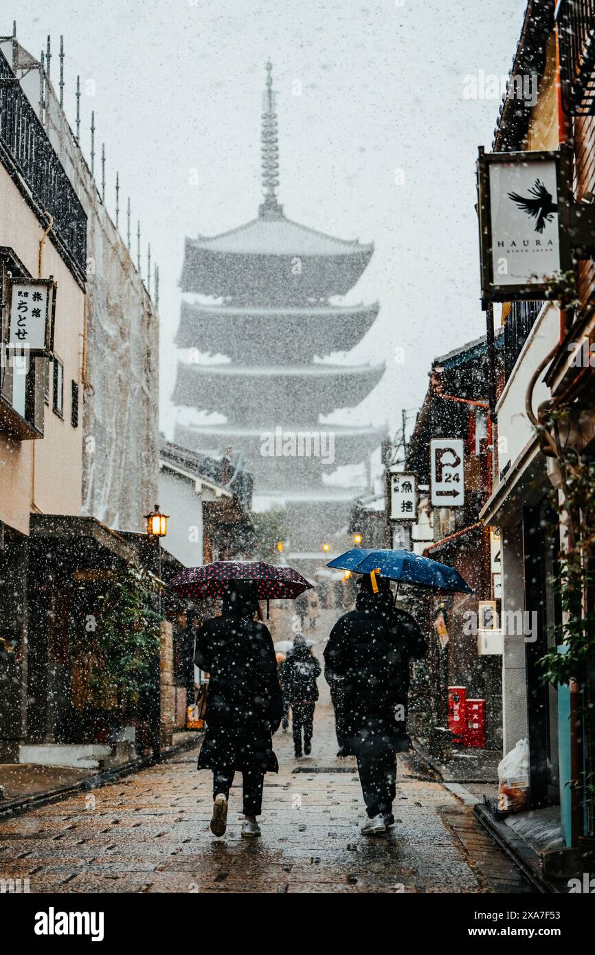 Zwei Personen mit Sonnenschirmen spazieren durch eine urbane Gasse Stockfoto