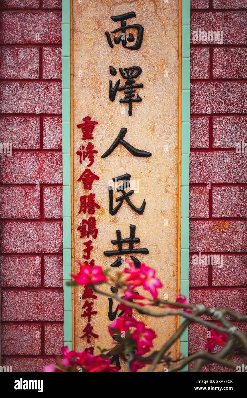 Eine Steinmauer mit asiatischen Charakteren und blühenden Blumen Stockfoto