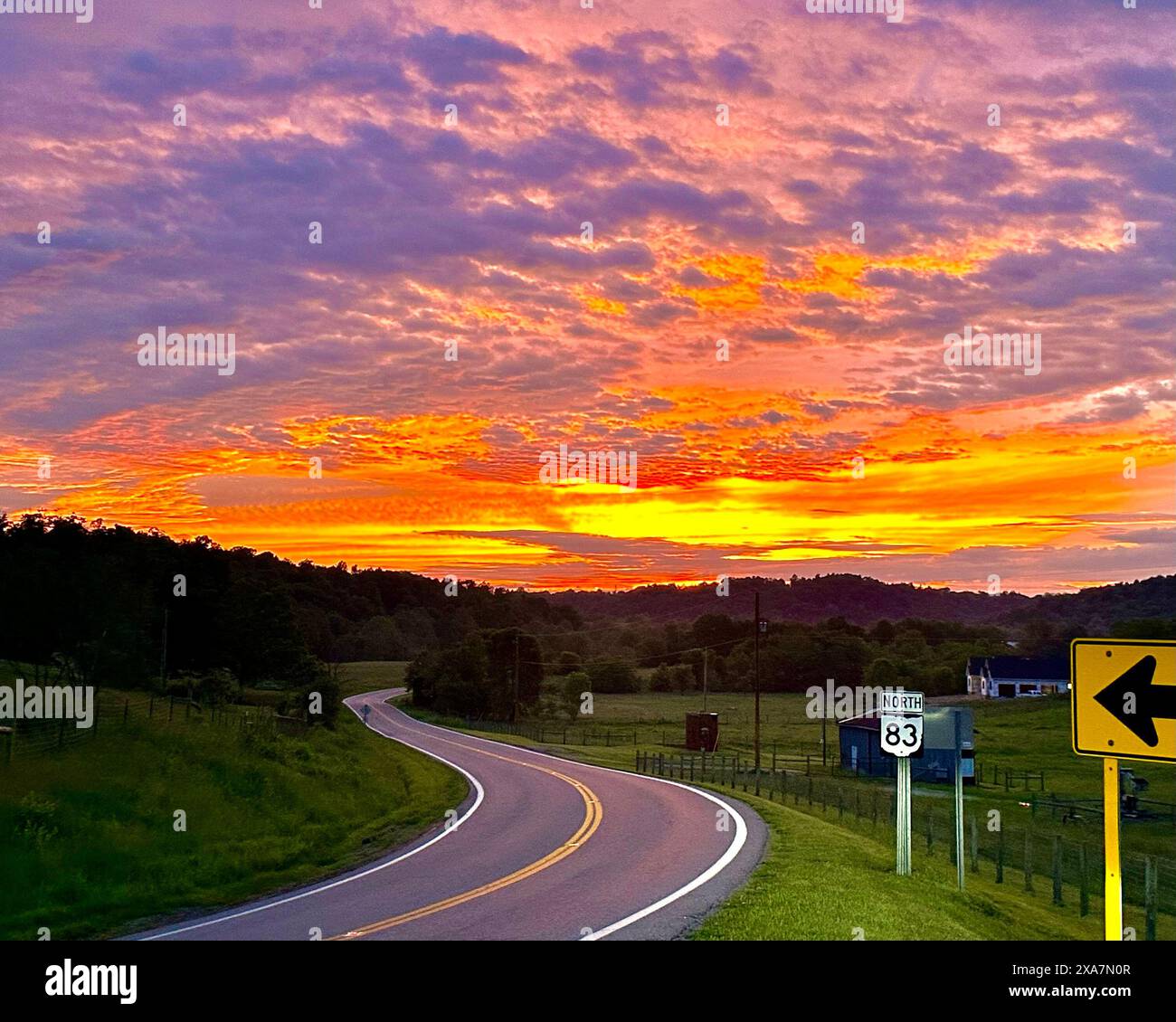 Ein wunderschöner Sonnenuntergang mit einem Pfeil, der auf eine Autobahn zeigt, die zum Sonnenuntergang führt Stockfoto