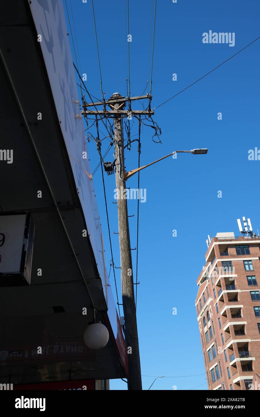 Ein hölzerner Strommast mit Stromleitungen und einer Straßenlaterne erhebt sich über einer Markise in einem klaren blauen Himmel in der King Street, Newtown, Sydney Stockfoto