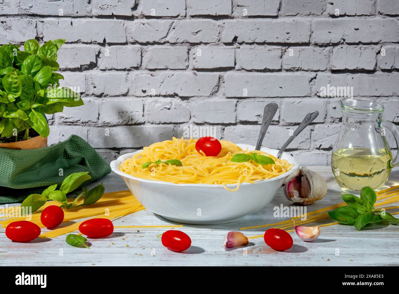 Schüssel mit gekochten Spaghetti umgeben von Tomaten, Basilikum, Olivenöl und Knoblauch auf einem Tisch Stockfoto