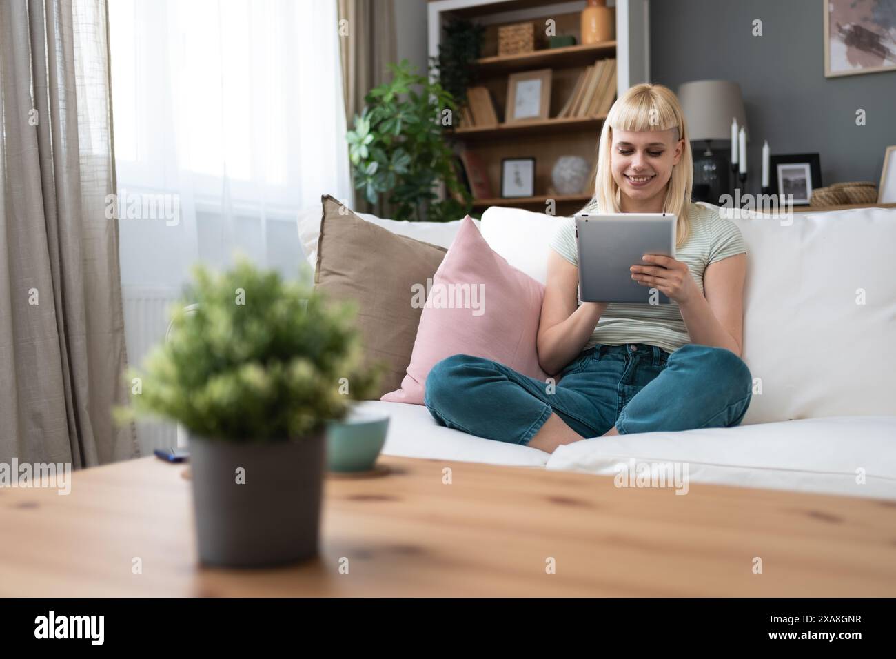 Junge Millennials Frau, die zu Hause auf dem Sofa mit digitalem Tablet sitzt, im Internet surft, Online-Dating-App, E-Mails liest oder Nutzer sozialer Medien, Online-Te Stockfoto