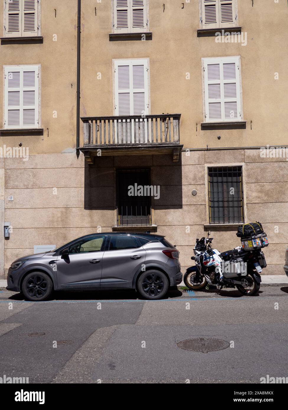 Cremona, Italien - 27. Mai 2024 Motorrad und Auto parken in einer leeren Straße in einer kleinen italienischen Stadt und genießen die Sommersonne. Stockfoto