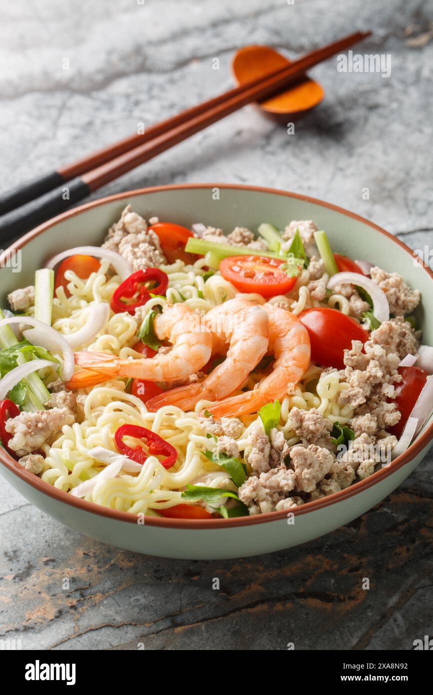 Thailändischer Salat mit Instant-Nudeln, Garnelen, Hackfleisch vom Schwein und Gemüse in einer Schüssel auf dem Tisch. Vertikal Stockfoto