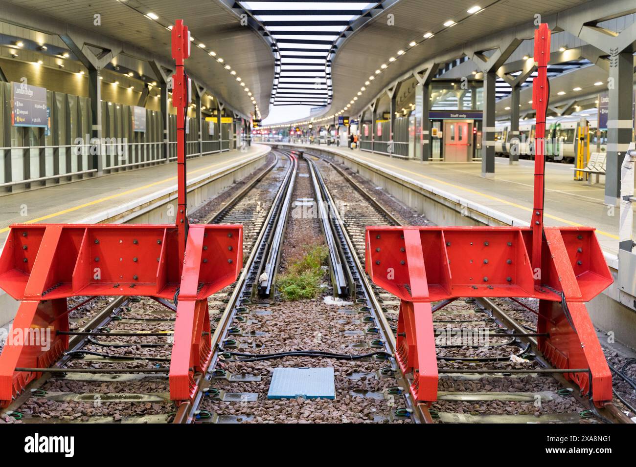 Zwei rote Haltestellen am Bahnsteig mit leeren Gleisen, die von den Scheinwerfern auf dem Dach des Bahnsteigs beleuchtet werden Stockfoto