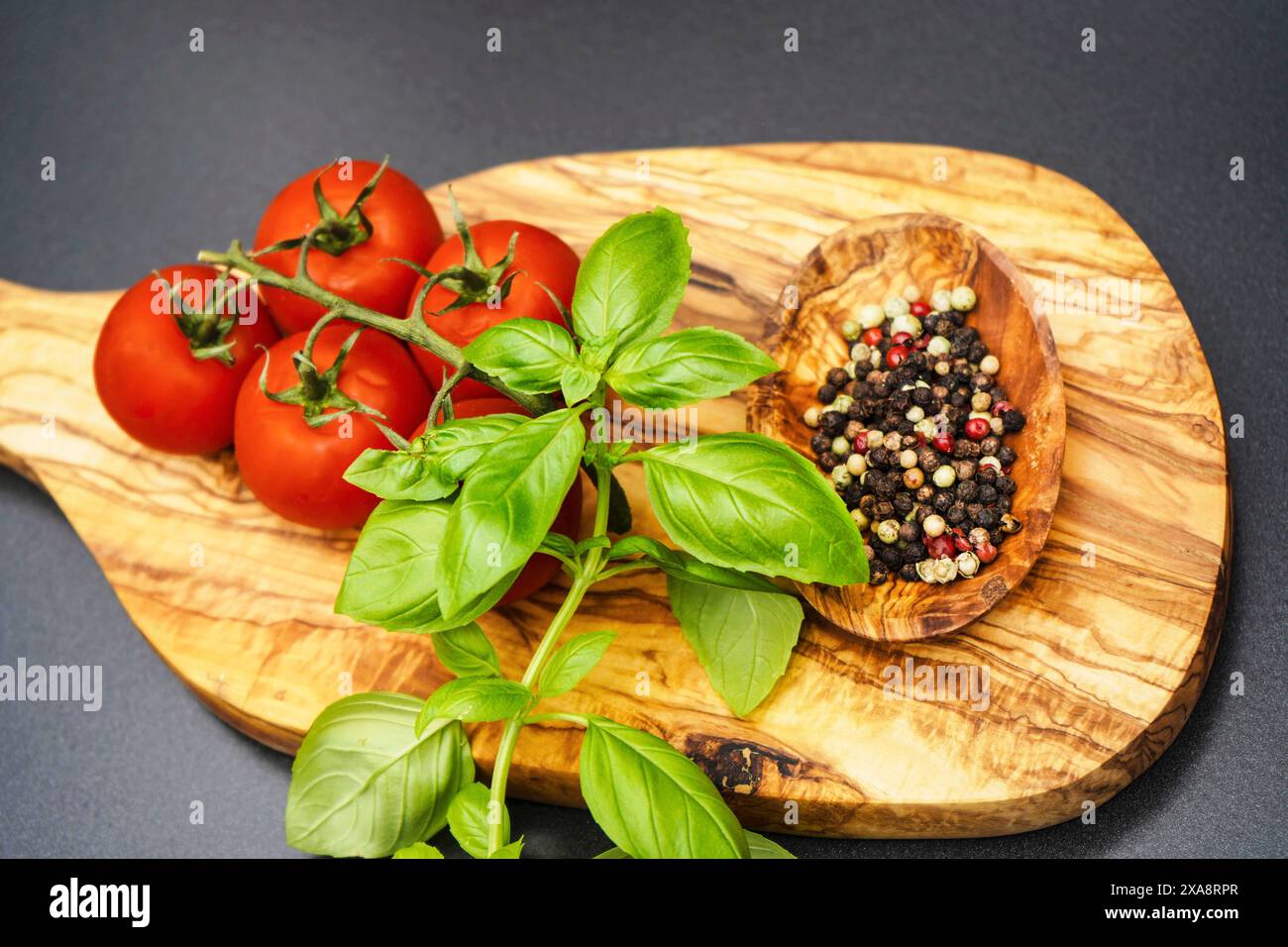 Olivenholzbrett mit Pfeffermischung, Tomaten und Basilikum Stockfoto