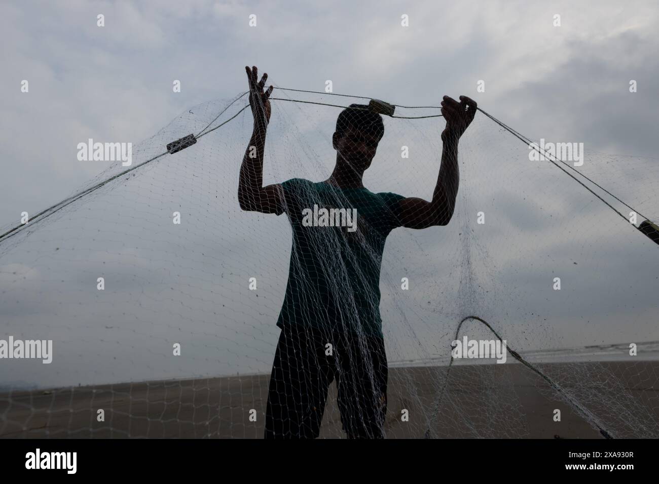 5. Juni 2024, Cox's Bazar, Chittagong, Bangladesch: Fischer, die Fischernetze für den Fischfang am Strand von Cox's Bazar in Bangladesch vorbereiten. Der Lebensunterhalt der Fischer hängt hier weitgehend von der Fischerei ab. Mit jedem Knoten und jeder Anpassung ehren sie eine zeitlose Tradition des Lebensunterhalts, die mit den Rhythmen der natürlichen Welt harmoniert. Cox's Bazar, der längste natürliche Meeresstrand der Welt, erstreckt sich über 120 km entlang der Südostküste Bangladeschs. Berühmt für seinen goldenen Sand, die pulsierenden Sonnenuntergänge und die sanfte Brandung, zieht es jährlich Millionen von Touristen an. (Bild: © Joy Stockfoto