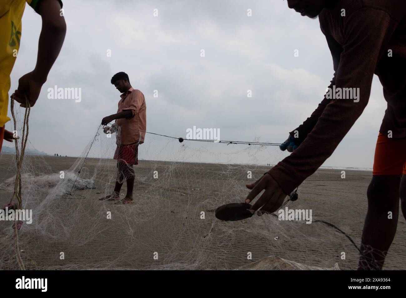 5. Juni 2024, Cox's Bazar, Chittagong, Bangladesch: Fischer, die Fischernetze für den Fischfang am Strand von Cox's Bazar in Bangladesch vorbereiten. Der Lebensunterhalt der Fischer hängt hier weitgehend von der Fischerei ab. Mit jedem Knoten und jeder Anpassung ehren sie eine zeitlose Tradition des Lebensunterhalts, die mit den Rhythmen der natürlichen Welt harmoniert. Cox's Bazar, der längste natürliche Meeresstrand der Welt, erstreckt sich über 120 km entlang der Südostküste Bangladeschs. Berühmt für seinen goldenen Sand, die pulsierenden Sonnenuntergänge und die sanfte Brandung, zieht es jährlich Millionen von Touristen an. (Bild: © Joy Stockfoto