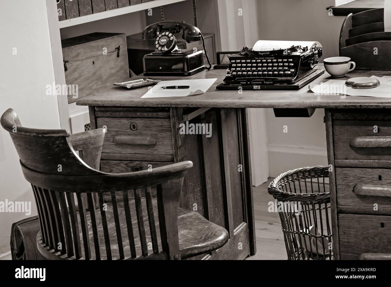 BÜRO 30er Jahre Vintage Schreibtischtelefon altes historisches Büro Innenraum Schreibtisch 1930er Jahre Technologie Ära Büro mit alten Stil Schreibtisch, Stuhl, Schreibmaschine und Retro schwarz Drehwählschalter Schreibtischtelefon, mit hölzernem Bürostuhl und verschiedenen Schreibtischpapieren usw. der Ära. Schwarzweiß-Sepia-Behandlung. 1920er/1930er Jahre Stockfoto