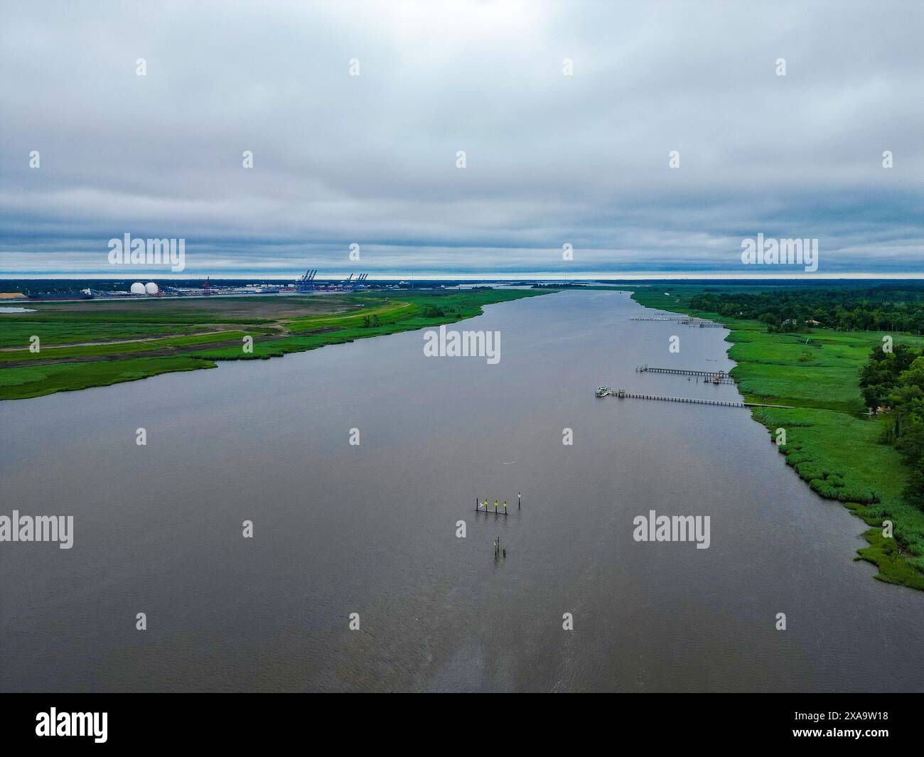 Ein Fluss, der an einem bewölkten Tag unter grauem Himmel durch grüne Felder fließt Stockfoto