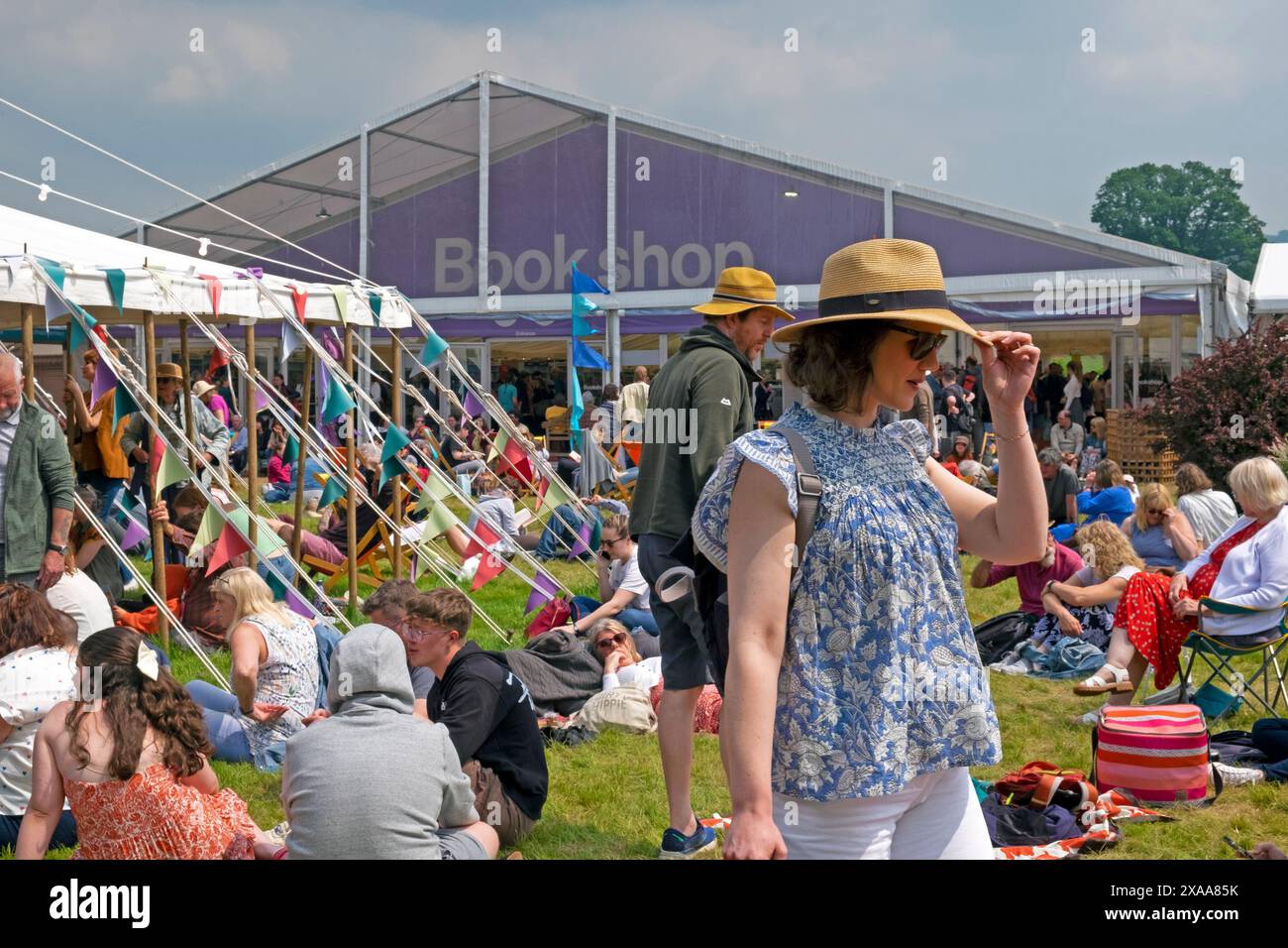 Junge Mode-Frau mit Strohhut und Sonnenbrille vor dem Buchladen auf der Hay Festival 2024 Website Hay-on-Wye Wales Großbritannien KATHY DEWITT Stockfoto