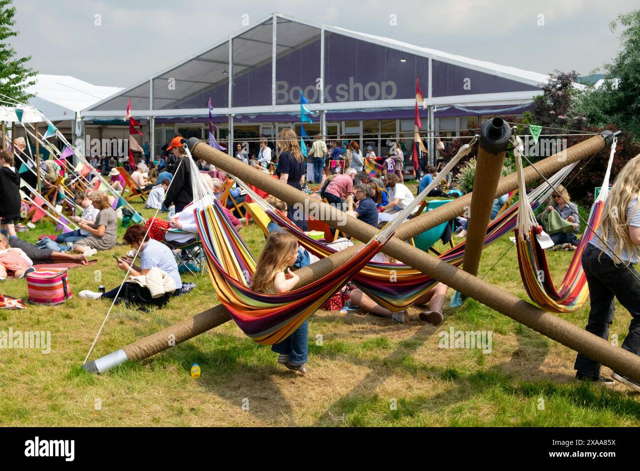 Kinder, die auf Hängematten spielen, Menschen in Gartenliegen vor dem Buchladen Marquis Hay Book Festival Hay-on-Wye Wales Großbritannien KATHY DEWITT Stockfoto