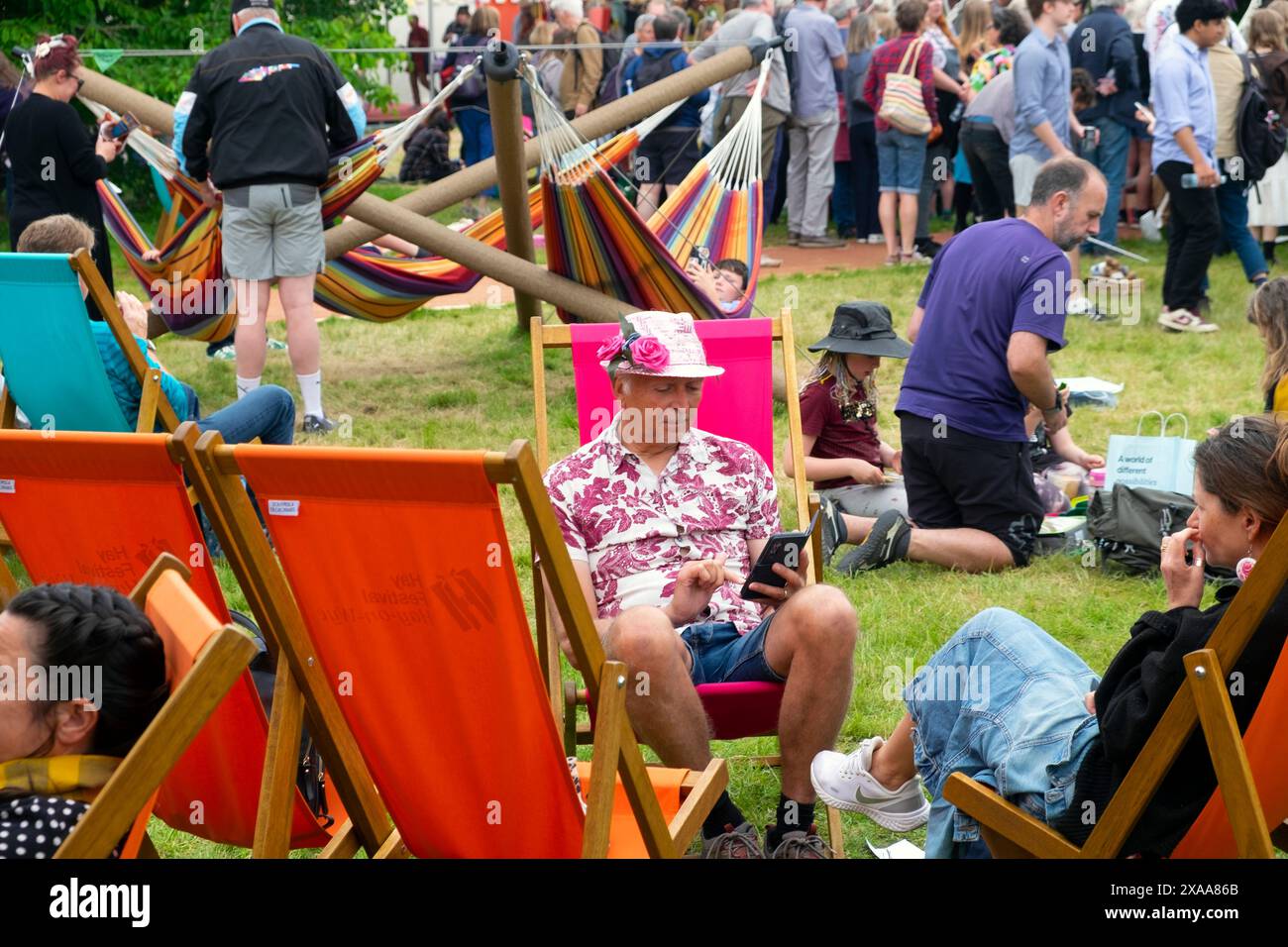 Menschen Besucher Mann mit Strohhut rosa Rose liest Buch in Liegestühlen auf der Hay Festival Website 2024 Hay-on-Wye Wales Großbritannien KATHY DEWITT Stockfoto