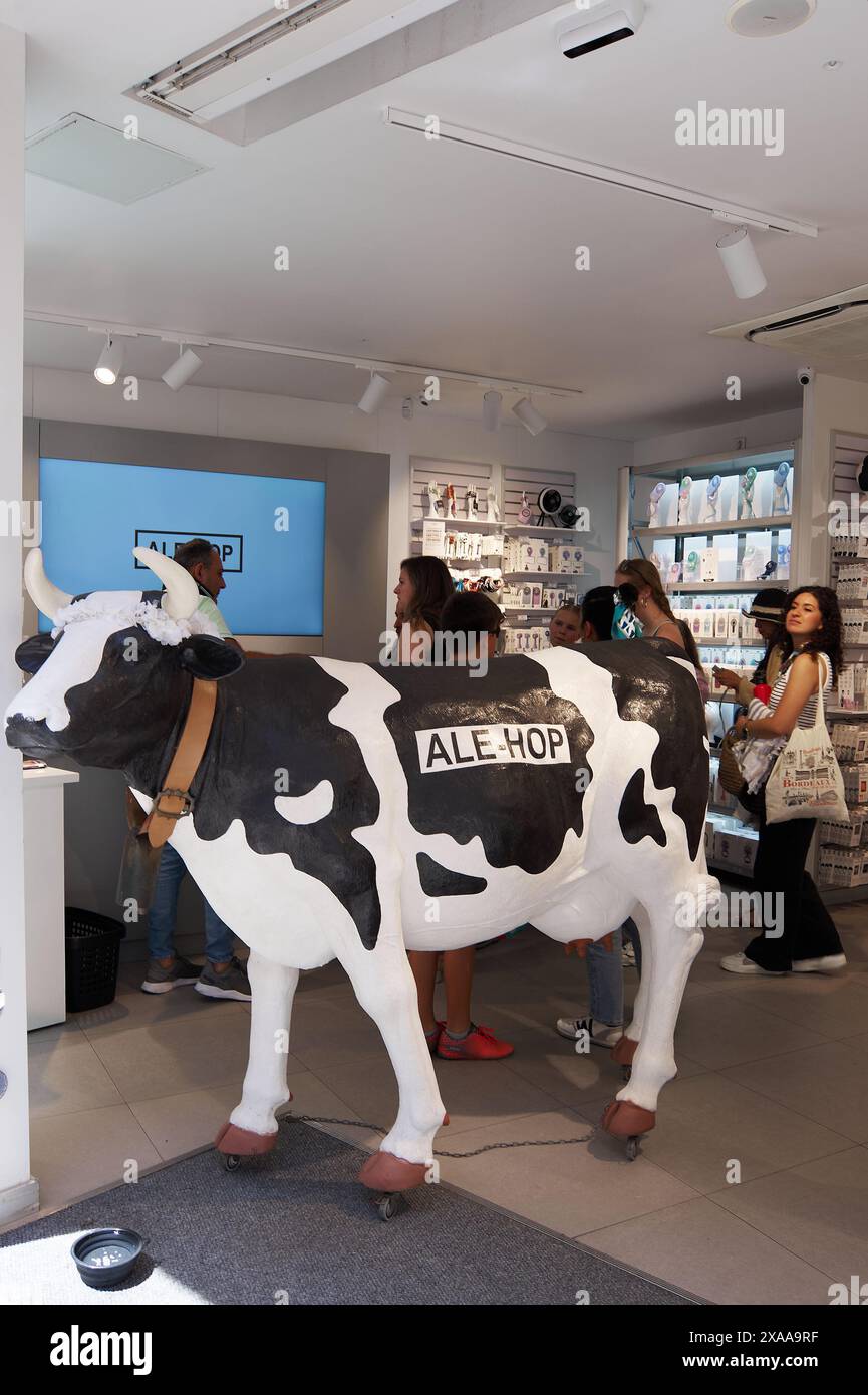 Sitges, Barcelona, Spanien-05. Juni 2024: ALE-Hop Souvenirladen mit einem Kuhmodell im Vordergrund, verschiedenen Produkten in Regalen und Kunden im Backgr Stockfoto
