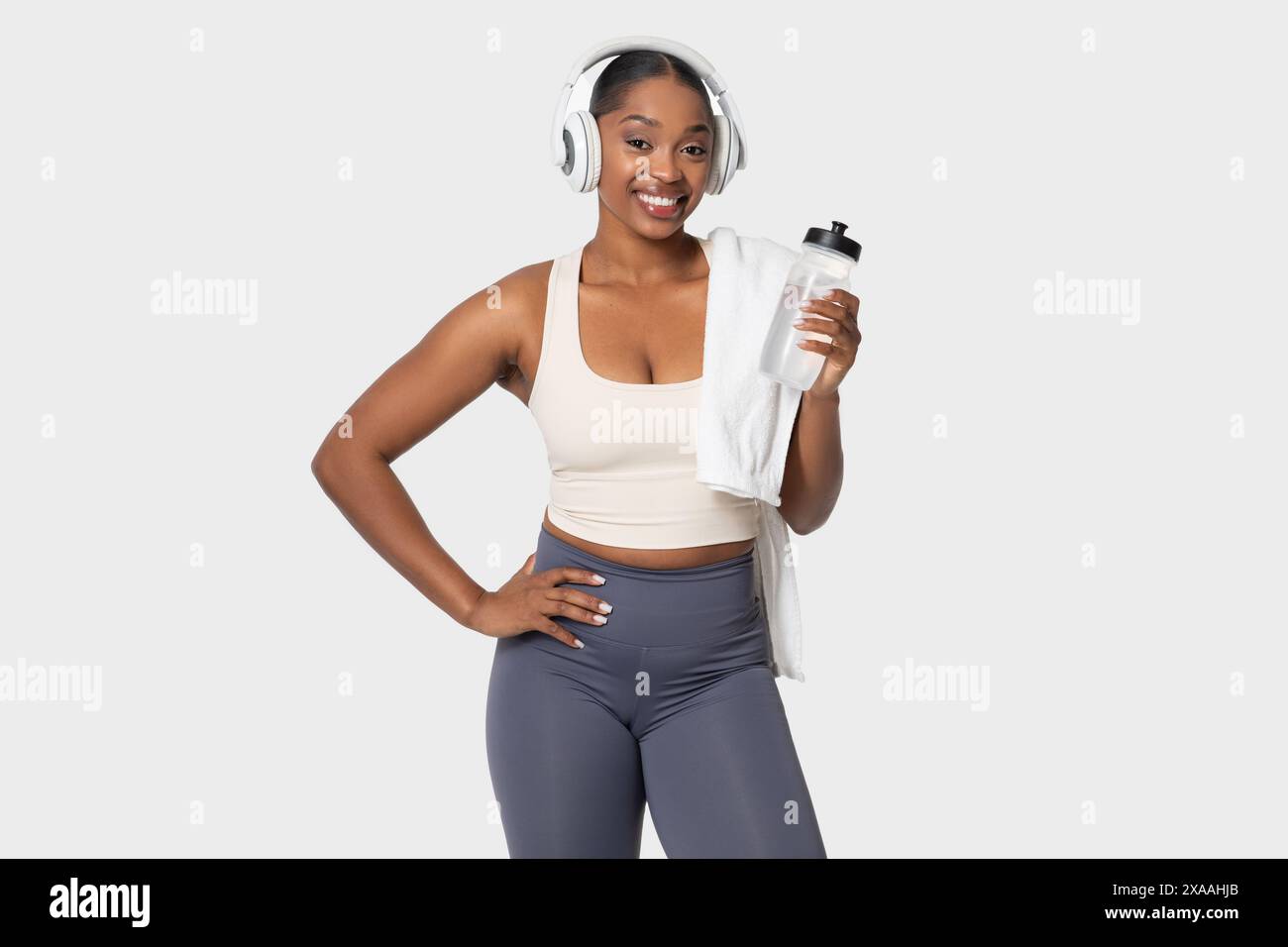 Frau in Workout-Kleidung, die eine Wasserflasche hält und Kopfhörer trägt Stockfoto