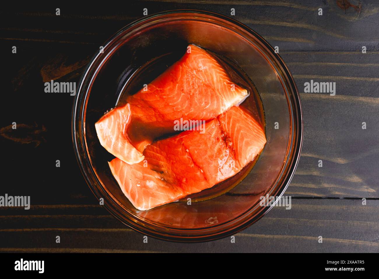 Marinieren von Lachsfilets mit der Hautseite nach unten: Rohe Lachsfilets in einer Glasschale mit der Hautseite nach unten mariniert Stockfoto