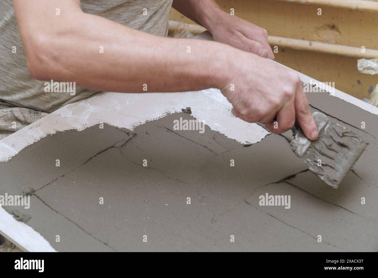 Ein Bauarbeiter bringt Zement mit einem Spachtel auf eine Keramikfliese auf. Weichzeichner. Selektiver Fokus Stockfoto