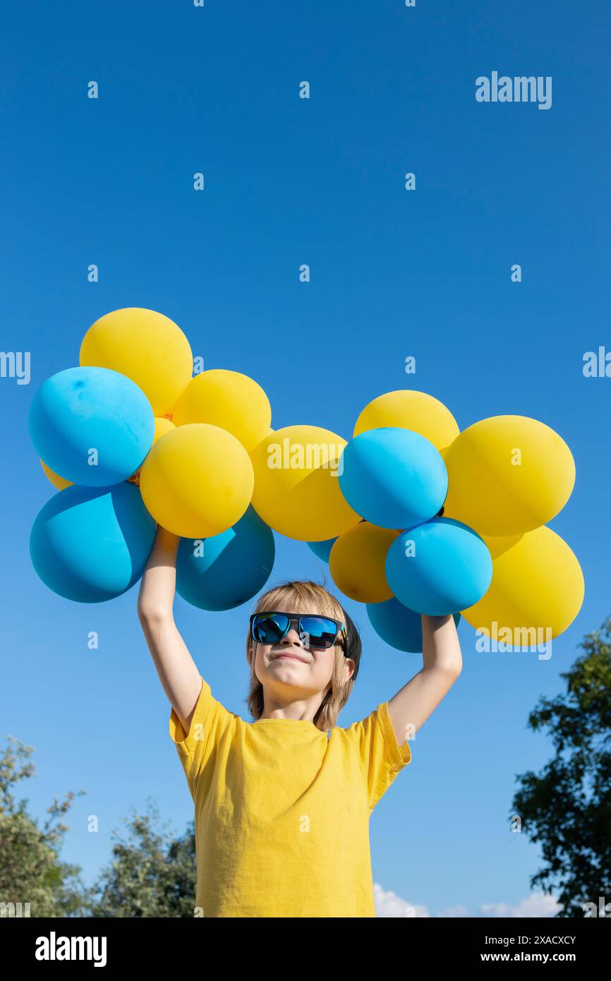 Junge mit vielen blauen und gelben Kugeln in den Händen auf dem Hintergrund des Himmels. Stoppt den Krieg. Glücklicher Kinderstand mit der Ukraine. Gute Laune, Geburtstag. Indepen Stockfoto