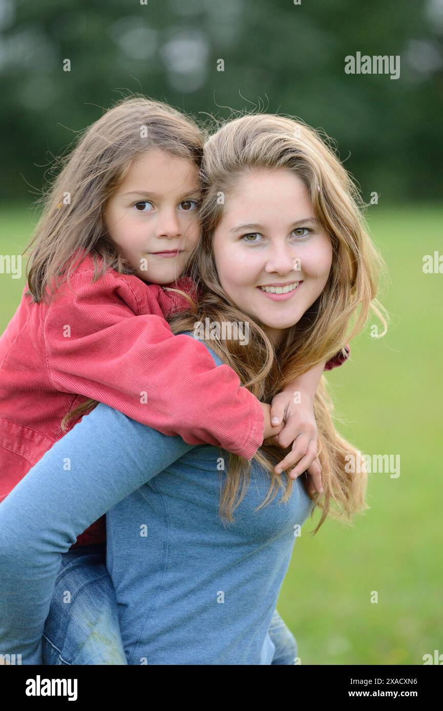 Das Mädchen trägt ihre kleine Schwester mit Huckepack im Freien, Deutschland Stockfoto