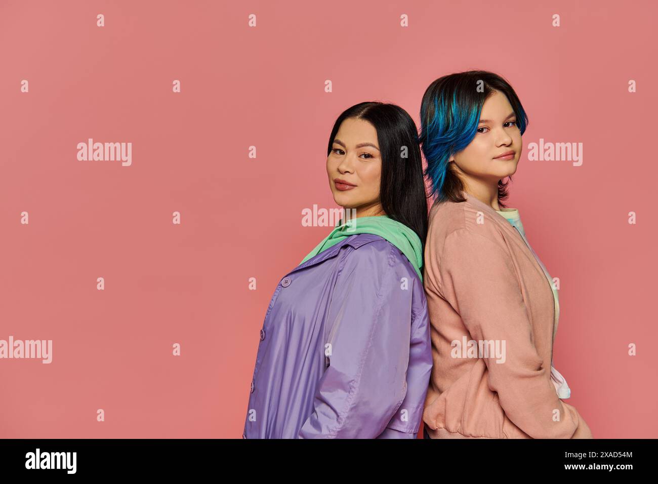 Eine stilvolle asiatische Mutter und ihre Teenager-Tochter, beide mit leuchtend blauen Haaren, posieren zusammen auf einem rosa Studiohintergrund. Stockfoto