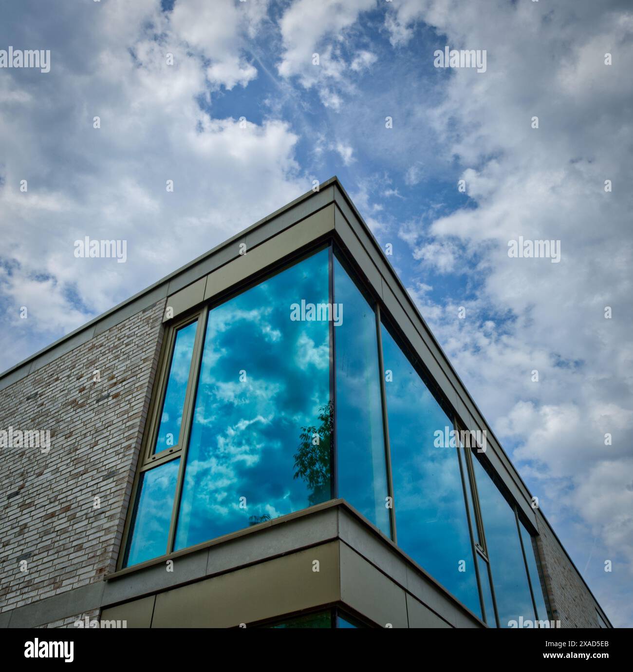 Ecke eines modernen Gebäudes mit grünen Fenstern, die die Wolken am Himmel reflektieren Stockfoto