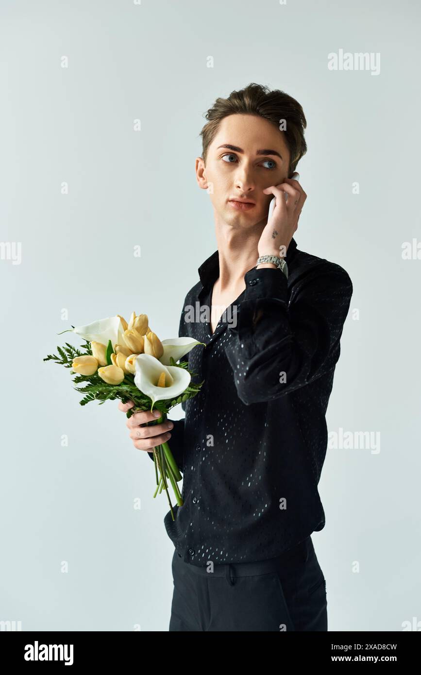 Eine junge queere Person ist Multitasking und spricht am Telefon, während sie in einem Studio einen Blumenstrauß hält. Stockfoto