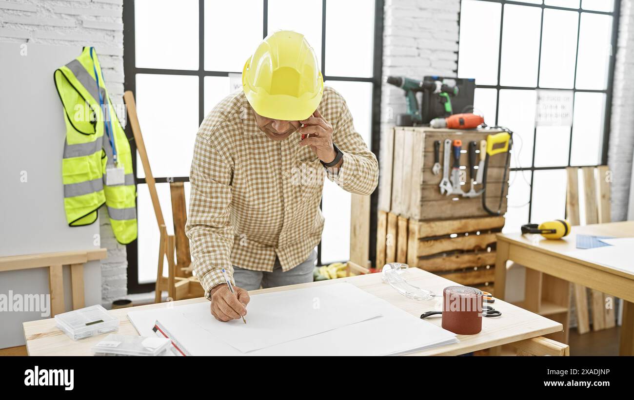 Hispanischer Zimmermann mit Hardhat, der Pläne am Telefon in der Werkstatt diskutiert Stockfoto
