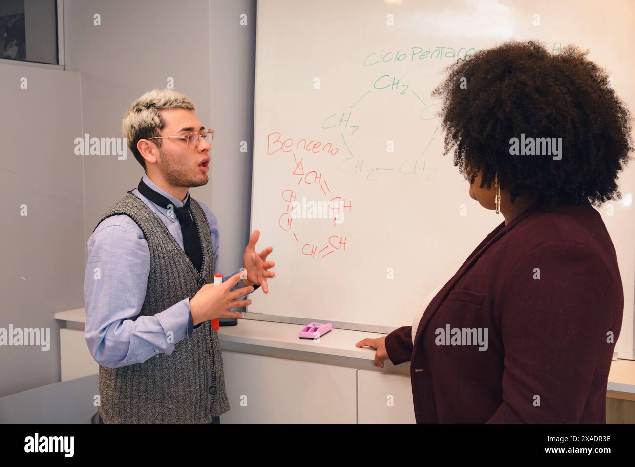 Ein junger Mann und eine Frau stehen vor einem Whiteboard mit chemischen Formeln. Der Mann redet mit der Frau, und das scheint sie zu sein Stockfoto