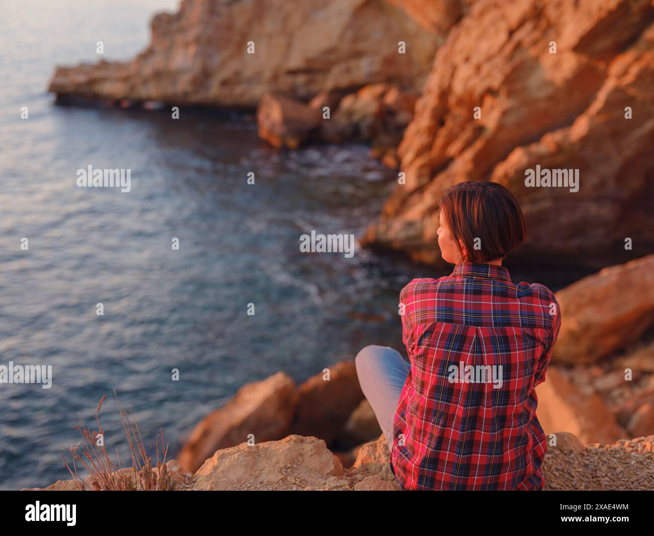 Junge Frau wandert am felsigen Strand in Spanien, Benidorm. Beobachten Sie das abgehackte Meer und die Bucht. Reisende genießen Freiheit in einer ruhigen Naturlandschaft Stockfoto