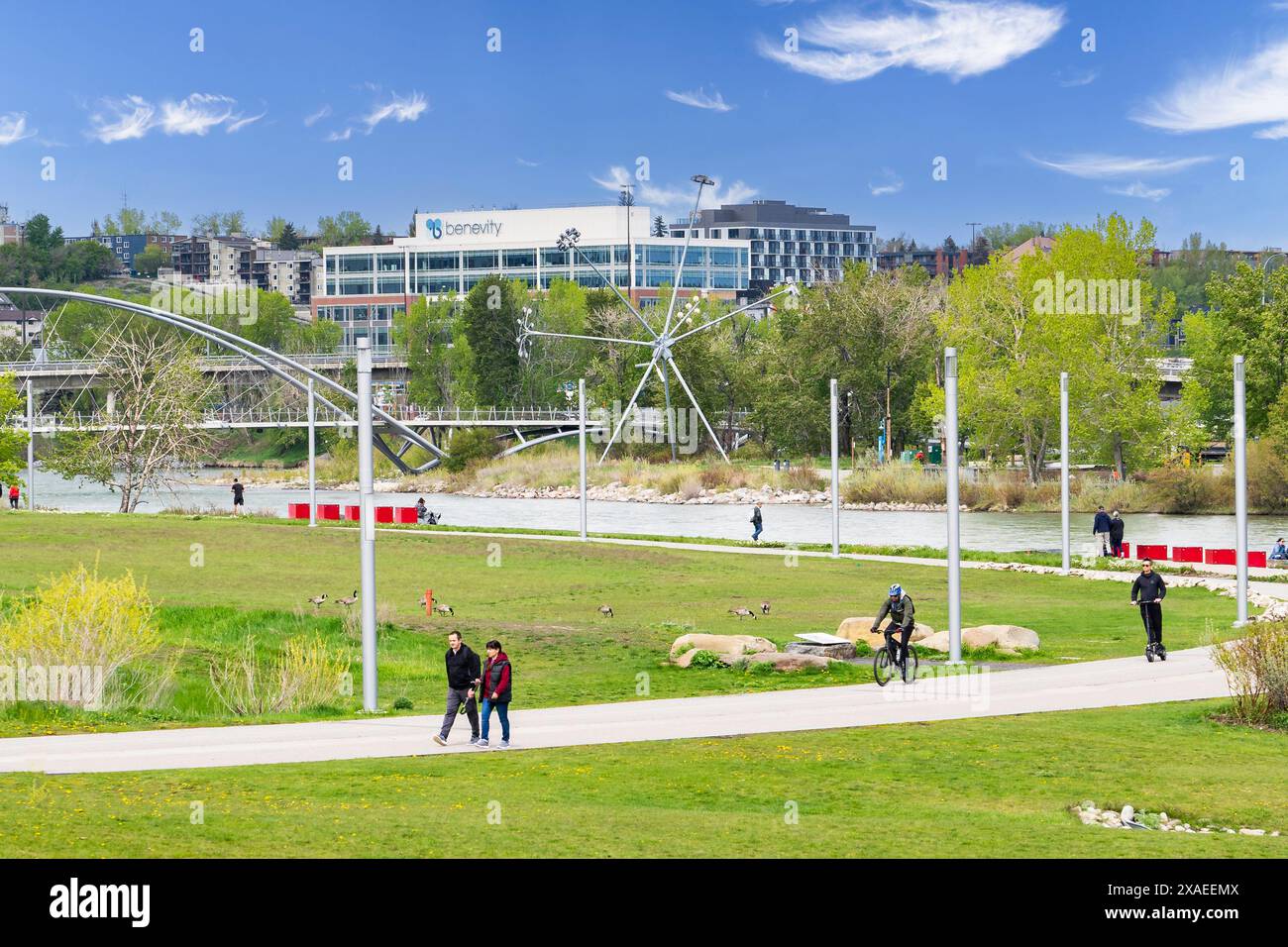 Calgary Alberta Canada, Mai 30 2024: Fußgänger und Radfahrer nutzen einen Fußweg entlang eines Flusses mit Blick auf einen Stadtpark in East Village. Stockfoto