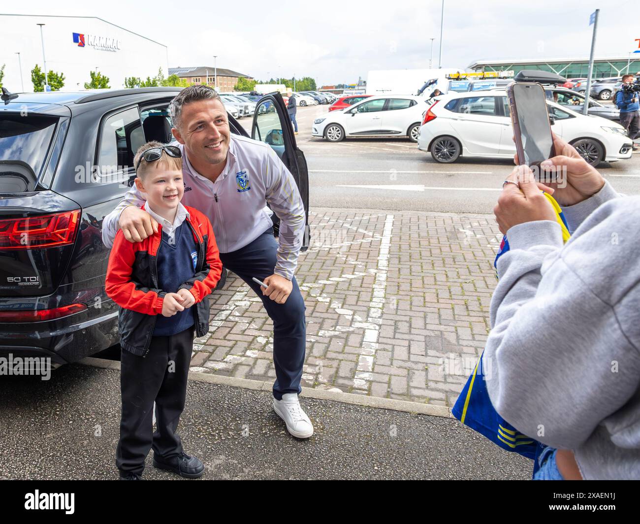 Warrington, Cheshire, Großbritannien. Juni 2024. Warrington Wolves verließ das Halliwell Jones Stadium am 6. Juni 2024 und zog in Richtung Wembley Stadium, um das Finale des Rugby Football League Challenge Cup gegen Wigan zu erreichen. Die Unterstützer waren da, um sie abzuhauen. Manager Sam Burgess nahm sich die Zeit, sich mit einem jungen Unterstützer ein Foto machen zu lassen. Quelle: John Hopkins/Alamy Live News Stockfoto